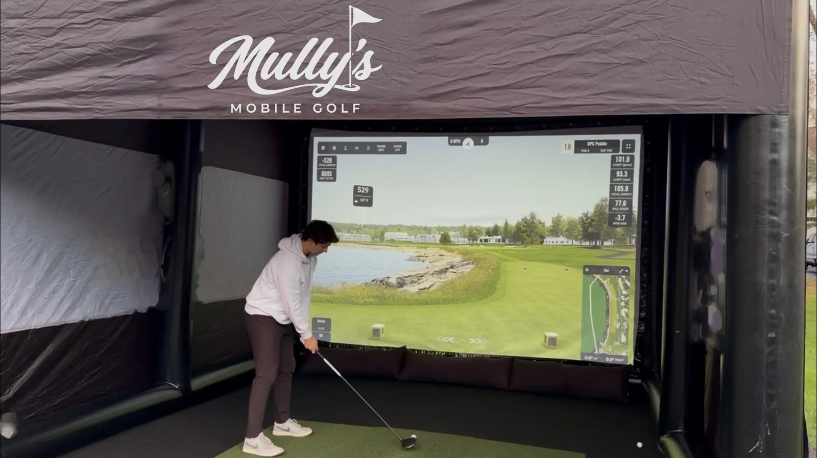 A golfer lining up a drive inside the Mully's simulator, a coastal hole on the big screen